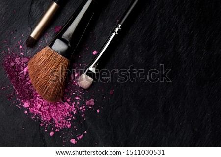 Make-up brushes with crushed cosmetics, shot from above on a black background with copyspace, a beauty design template for a makeup banner