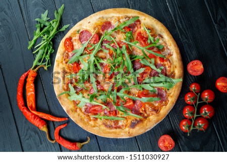 Homemade fresh Pizza with salami, pepperoni cherry tomatoes and arugula on a black wooden with copy space. Top view food photo. Flat lay. Italian cuisine. Hot, spicy pizza