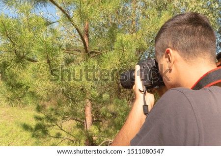 A man in an attempt to take a good picture of a fir. Outdoor background. Seasonal shot. Equipment for taking pictures. Favorite job. 