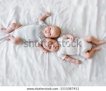 Two twin boys are lying on a large bed head to head but legs in different directions. The picture is taken from above vertically above them.