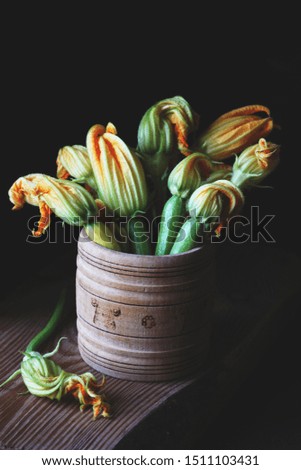 Dark and moody photo of yellow and green zucchini and squash blossoms in a wooden bowl on a dark background taken using natural light
