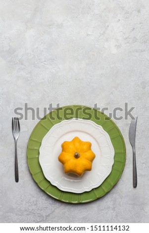 Seasonal empty serving plate at gray concrete background with fork ad knife and decor pumpkin. Concept of harvest and crop table set. Thanksgiving and halloween serving plate. Top view