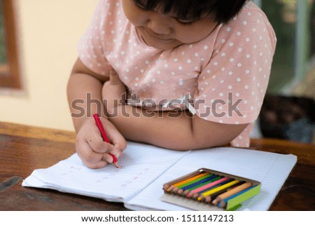 Close up of girl hand with pencil writing english words by hand on  white notepad paper at white background, A child is holding a crayon in his hands at paper and crayons for drawing
