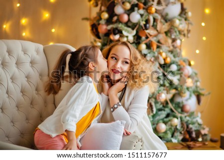 daughter kisses mom on the cheek near the Christmas tree