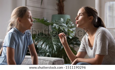 Caring young mom sit at home study with daughter stutter pronounce sounds, loving mother parent speak teach impaired disabled child, do exercises practice voice pronunciation and articulation together Royalty-Free Stock Photo #1511190296