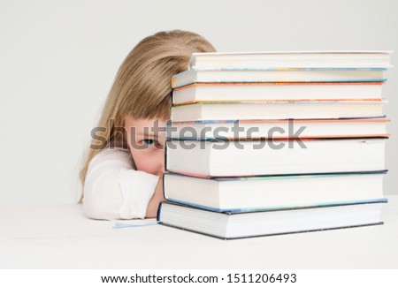 Beautiful little girl hiding behind a stack of books; neutral bacground