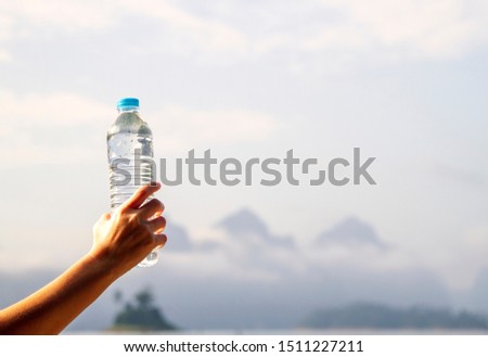 Close up of hand holds a bottle of purify water with background of beautiful nature with copy space Royalty-Free Stock Photo #1511227211