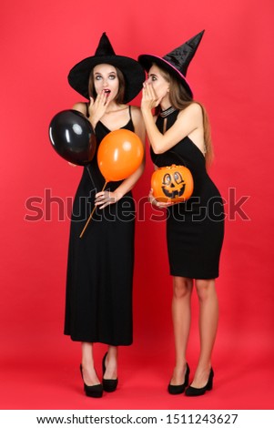 Two young women in halloween costumes with balloons and pumpkin bucket on red background