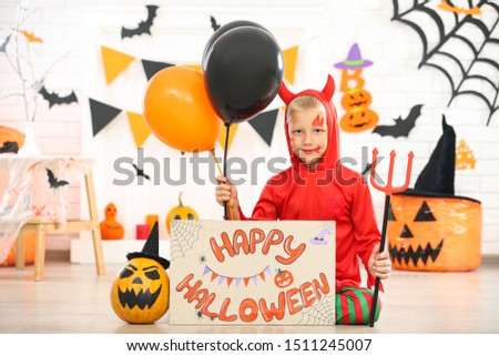 Young boy in costume holding balloons and paper with text Happy Halloween