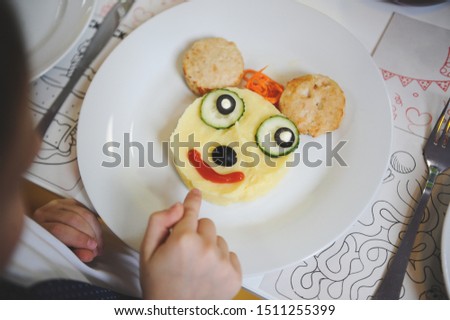 little boy pointing his finger at plate with funny tasty dish with cartoon character face from food