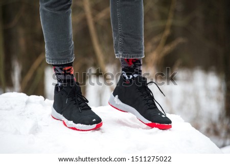 Male legs in athletic shoes, cropped jeans and fashionable socks standing on snow.  Stylish and trendy winter look.