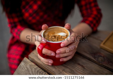 delicious aromatic coffee in a red cup in the hands of a girl who is sitting in a cafe