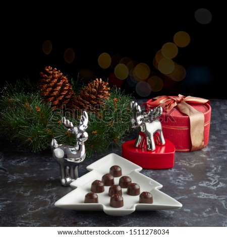 Plate in the form of a Christmas tree with chocolates on the background of figures of Christmas reindeer, gifts and a wreath with cones. space for your text.