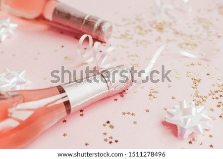 Christmas or New Year composition with bottles of rose champagne and golden shiny sparkle star confetti on pastel pink background, side view. Party Celebration creative concept