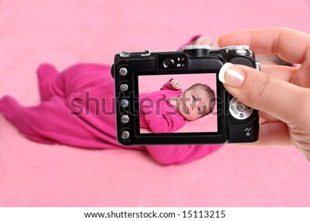 woman takes snapshot of a small one week old newborn baby girl on a pink background