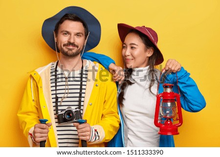 Photo of two friends have traveling, enjoy spending free time together, being experienced tourists, search for proper route, hold kerosene lamp, trekking sticks and retro camera, wear casual clothes