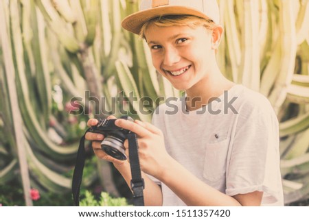 Young smiling tourist watching pictures in his mirrorless camera during holiday. Trendy child playing with fotocamera in an exotic context. Teen shooting travel memories. Traveling, tourism, concept.