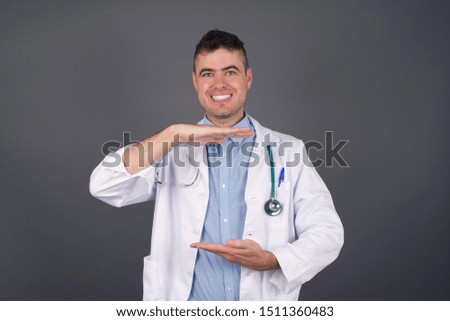 Young beautiful doctor man in medical uniform gesturing with hands showing big and large size sign, measure symbol. Smiling looking at the camera. Measuring concept.
