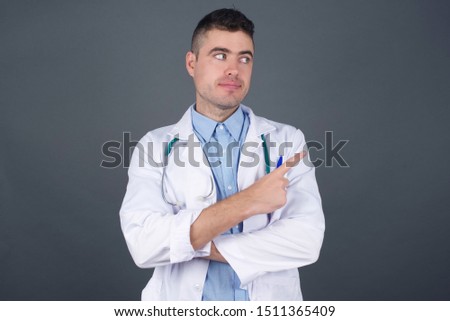Young doctor man over isolated background approving doing positive gesture with hand, thumbs up smiling and happy for success. Looking at the camera, winner gesture.