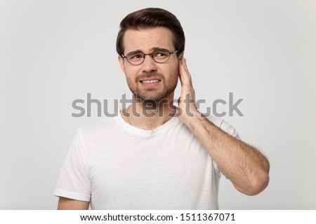 Unhealthy young man in eyeglasses touching ear, suffering from sudden throbbing ear ache, looking aside, head shot. Upset millennial guy feeling unwell, isolated on grey white studio background. Royalty-Free Stock Photo #1511367071