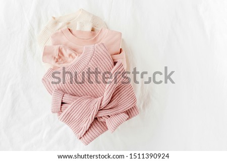 Three pale pink and white warm sweaters on bed. Women's stylish autumn or winter clothes. Cozy Winter look.  Flat lay, top view.