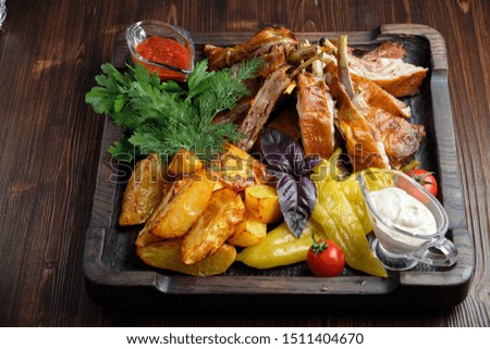 Barbecue on the bones with vegetables and potatoes on a black plate on a dark wooden background. catering menu