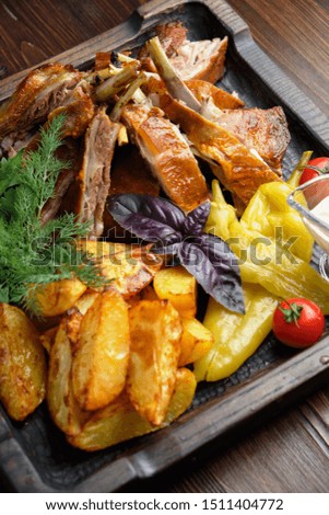 Barbecue on the bones with vegetables and potatoes on a black plate on a dark wooden background. catering menu