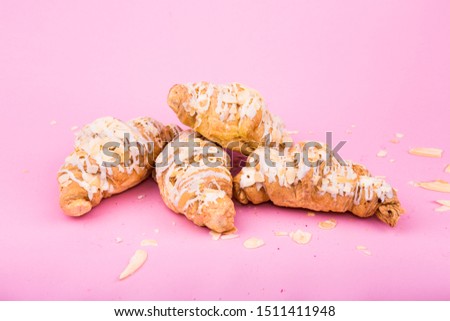 Delicate croissants with nuts and almonds on a pink background.