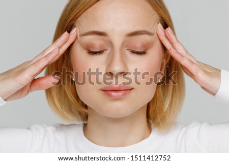 Woman meditating and massaging her temples, closes eyes, relieves emotional stress and nervous tension, exhausted from overwork, isolated on grey background. Fatigued worker suffering from headache. 