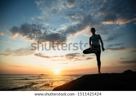 Woman doing exercises on the ocean during amazing sunset.
