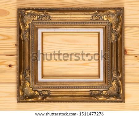 Ornate gold picture frame isolated on on a wooden background.