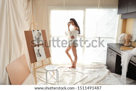 full length asian woman artist in white shirt drinking coffee while drawing picture with pencil (woman lifestyle concept)