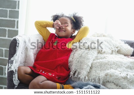 Portrait of a cute and shy little African girl, leaning back leaning against the sofa