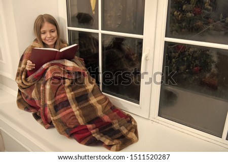 Magic xmas spirit. Little girl enjoy reading Christmas story. Little child read book on Christmas eve. Little reader wrapped in plaid sit on window sill. Childrens picture book. Winter wonderland.