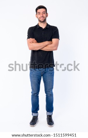 Full body shot of happy young bearded Persian man smiling with arms crossed