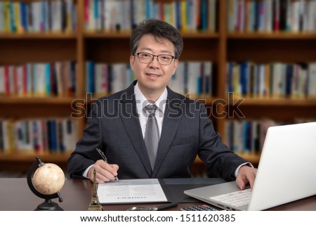 A portrait of an Asian middle-aged male businessman sitting at a desk. Royalty-Free Stock Photo #1511620385