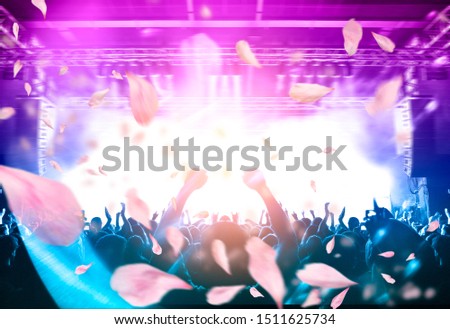 Concert crowd under a rain of confetti from above, background is a lit stage