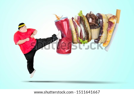 Picture of young fat man wearing sportswear while kicking soft drink and fast food