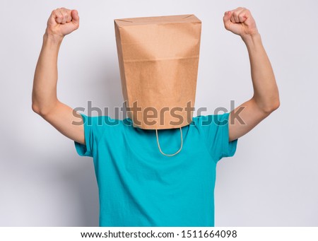 Portrait of teen boy with paper bag over head showing winning gesture. Successful and celebrating victory, triumphant child making win sign. Teenager cover head with bag, isolated on white background