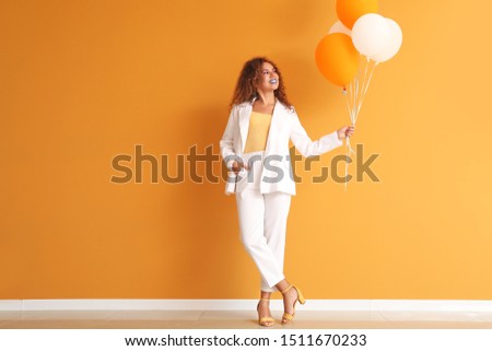Fashionable young African-American woman with balloons against color wall