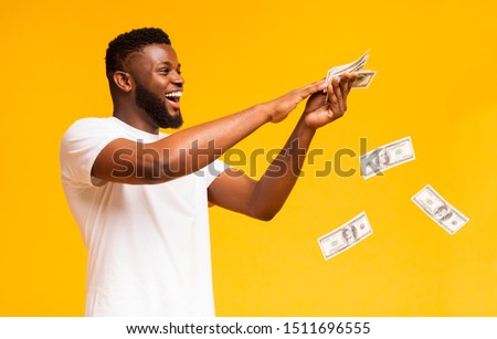 Happy african american man throwing out money banknotes, yellow studio background Royalty-Free Stock Photo #1511696555