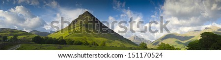 Dramatic mountain peak of Yewbarrow set against storm broken sky and warm hues of evening light, Lake District, Cumbria, UK. Royalty-Free Stock Photo #151170524