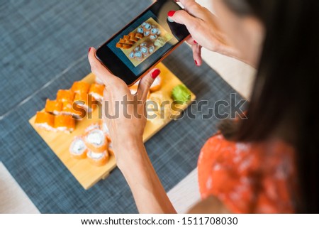 Girl takes pictures of sushi on phone. A girl takes pictures of sushi on the phone that lie on a black table
