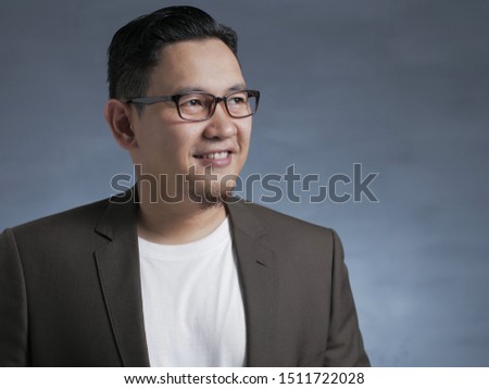Young Asian man with eyeglasses wearing white shirt and blazer, smiling expression, looking to the side with copy space. Close up body portrait