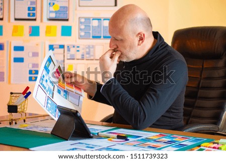 A man in black clothes chooses the color scheme for the mobile application. Mobile application designer in his office. Using the color palette in the designer's work.
