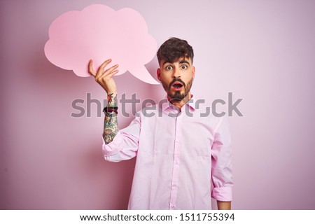 Young man with tattoo holding cloud speech bubble standing over isolated pink background scared in shock with a surprise face, afraid and excited with fear expression