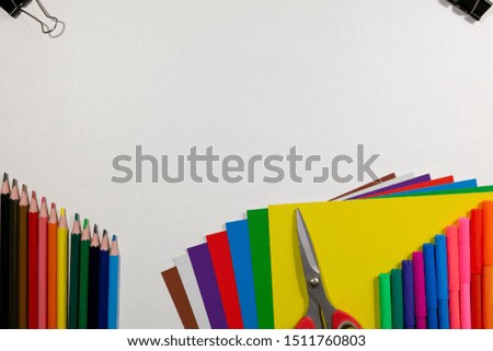 Children and school background. Colored paper, pencils, scissors and paper clip on white backdrop with a copy space in a middle. Top view, flat lay.