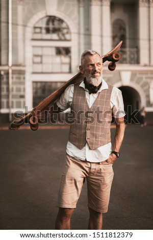 Adult bearded man portrait with longboard. Stylish model in casual clothes ride skateboard on city street background. Outdoors style. Sport lifestyle