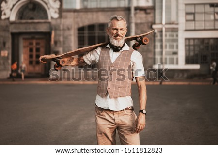 Stylish hipster bearded man with skateboard. Adult model in casual clothes ride longboard on city street. Street lifestyle sport photo Royalty-Free Stock Photo #1511812823