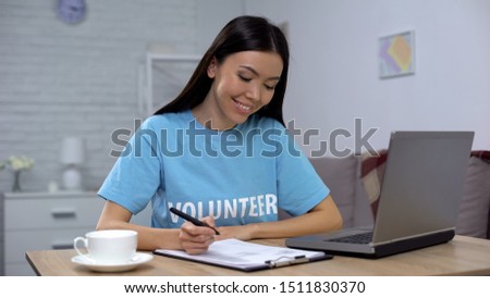 Female volunteer working laptop and writing notes sitting table, charity project